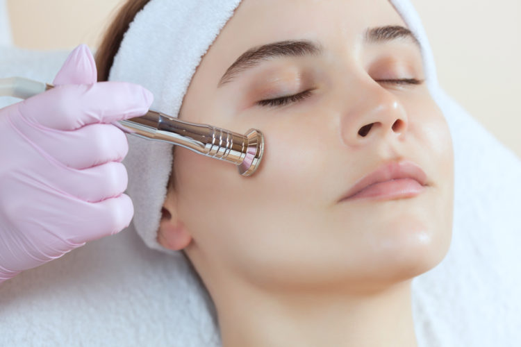 The cosmetologist makes the procedure Microdermabrasion of the facial skin of a beautiful, young woman